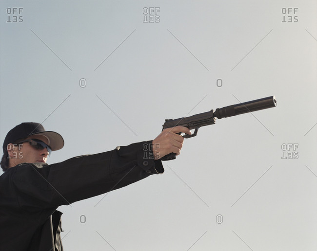 Man in special forces, aiming high powered hand gun with silencer attached