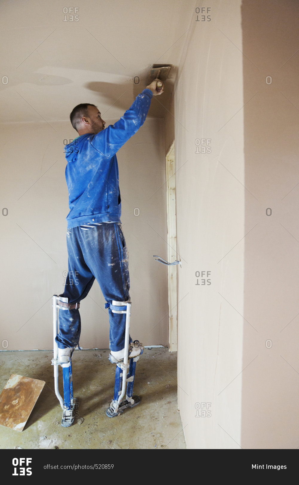 A plasterer wearing stilts smoothing fresh plaster high up on the walls