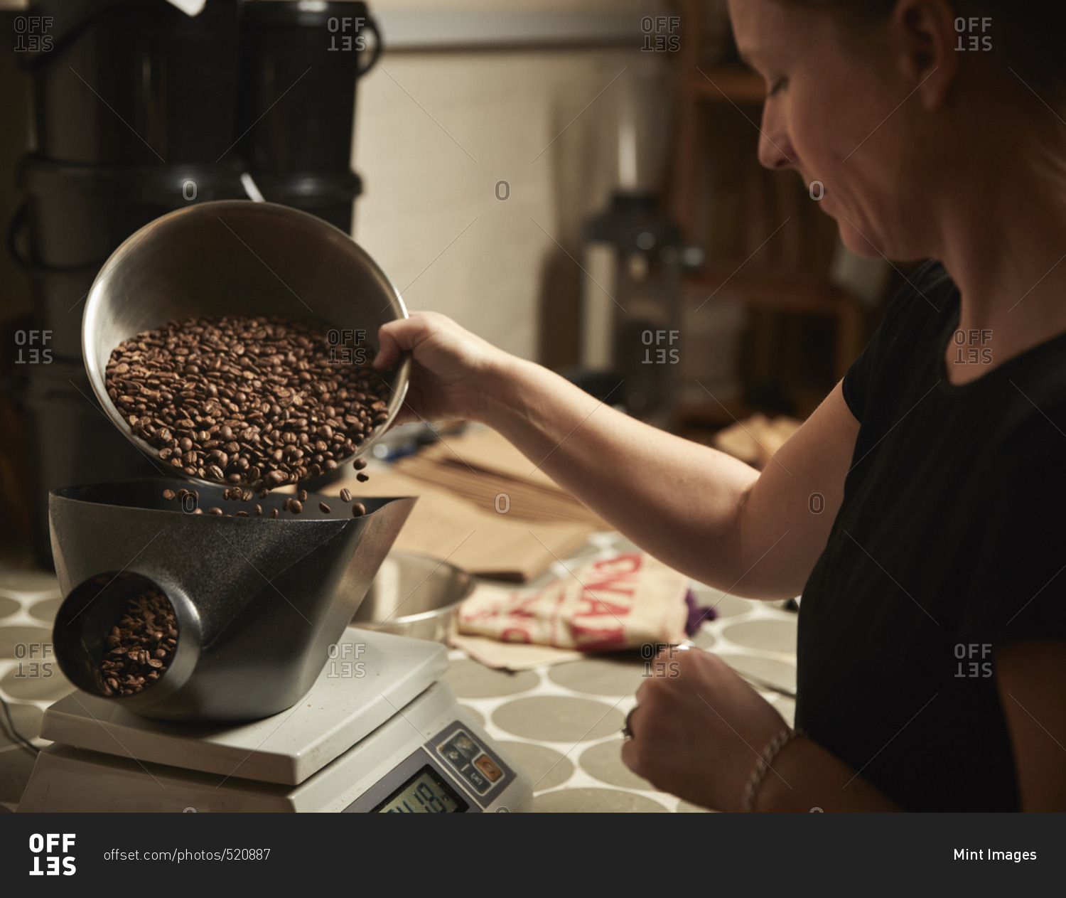 A coffee shop. A person pouring roasted coffee beans into a coffee grinder.