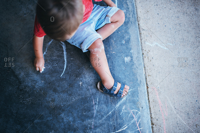 Boy sitting on sidewalk drawing
