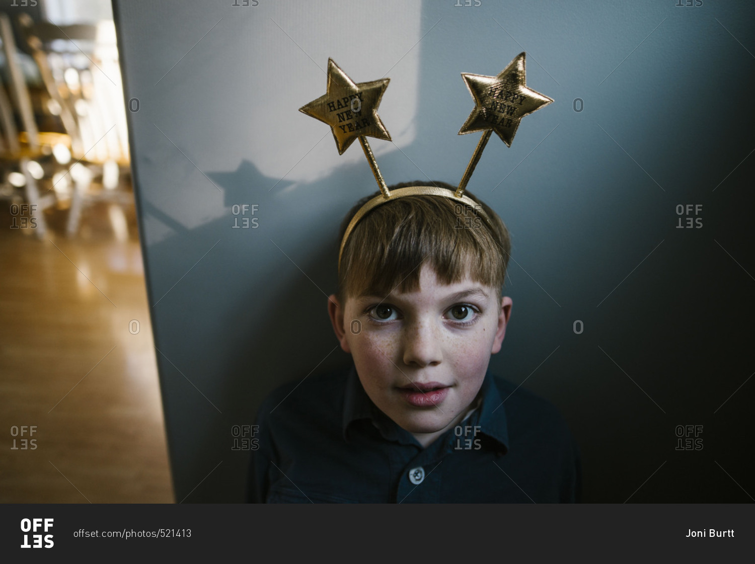 Boy wearing a Happy New Year headband leaning against a wall