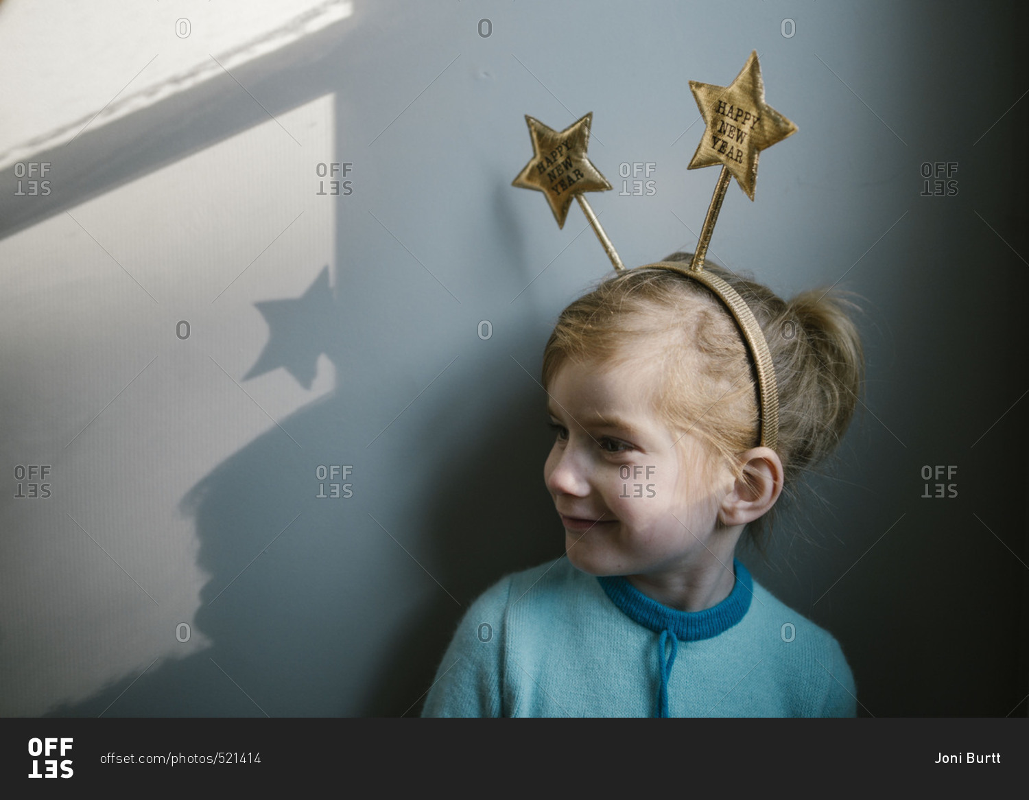 Little girl wearing a Happy New Year headband leaning against a wall