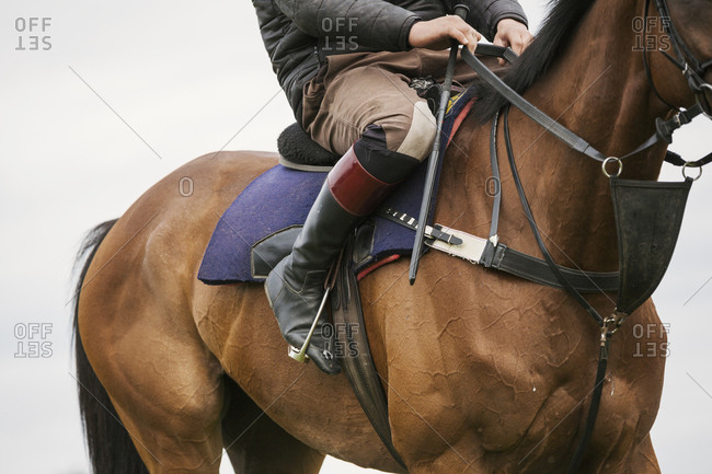 Close up of a rider wearing black riding boots riding a bay racehorse with short stirrups.