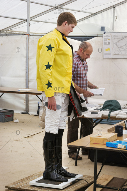Jockey in a yellow shirt standing on weighing scale, being weighed before a horse race.