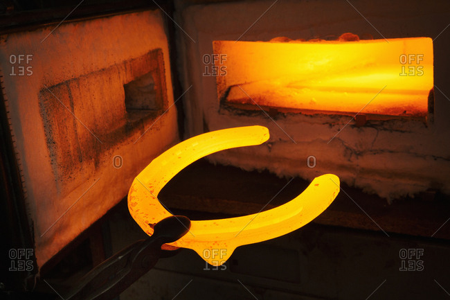A red glowing horseshoe shape, held with tongs, and an open furnace. Glowing heated metal.
