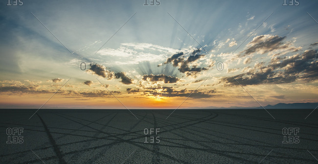 Tire tracks leading to the horizon in a desert landscape at dusk.