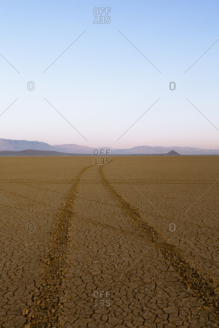 Tire tracks in a desert landscape with mountains in the distance.