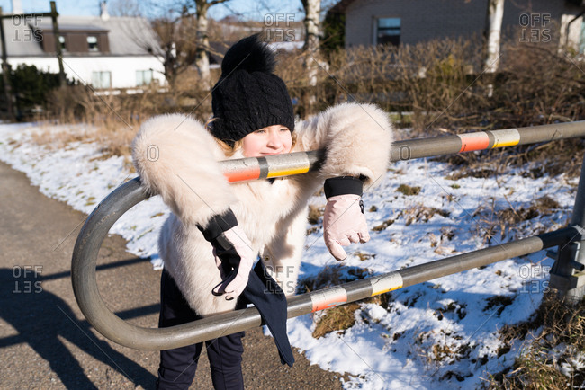 Girl in a furry coat leaning on a metal pedestrian guard rail