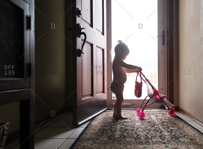 Toddler girl playing with doll stroller in doorway