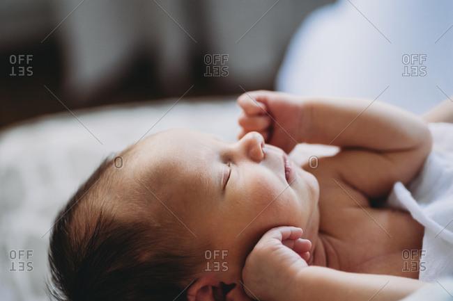 Newborn baby rests peacefully with arms raised to face