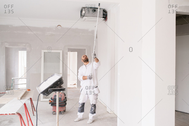 Painter using a long roller to paint the ceiling of a home