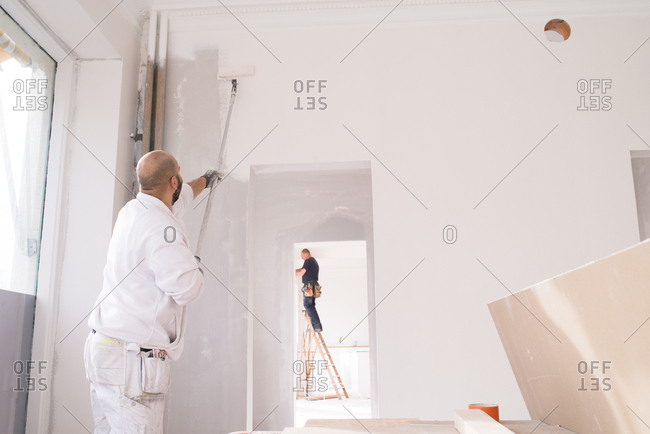Man painting the while of a house while an electrician works in another room