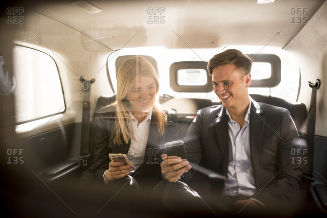Businessman and businesswoman using smartphone in black cab, London, UK