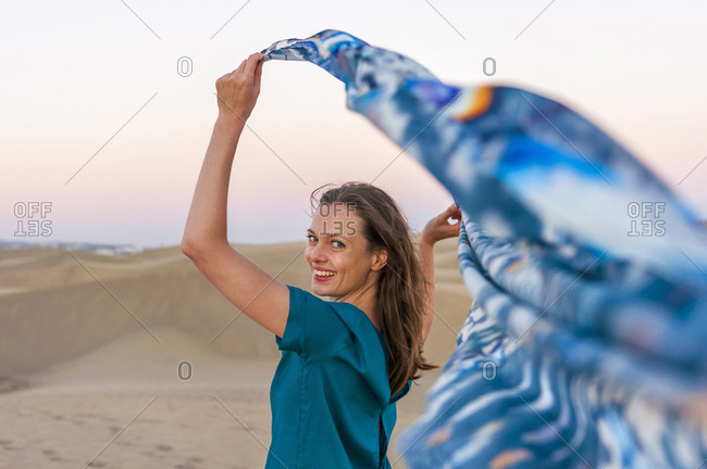 Woman on sand dunes, holding scarf out in breeze