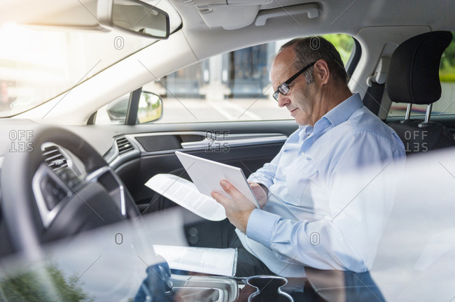 Senior male businessman updating paperwork and digital tablet in car