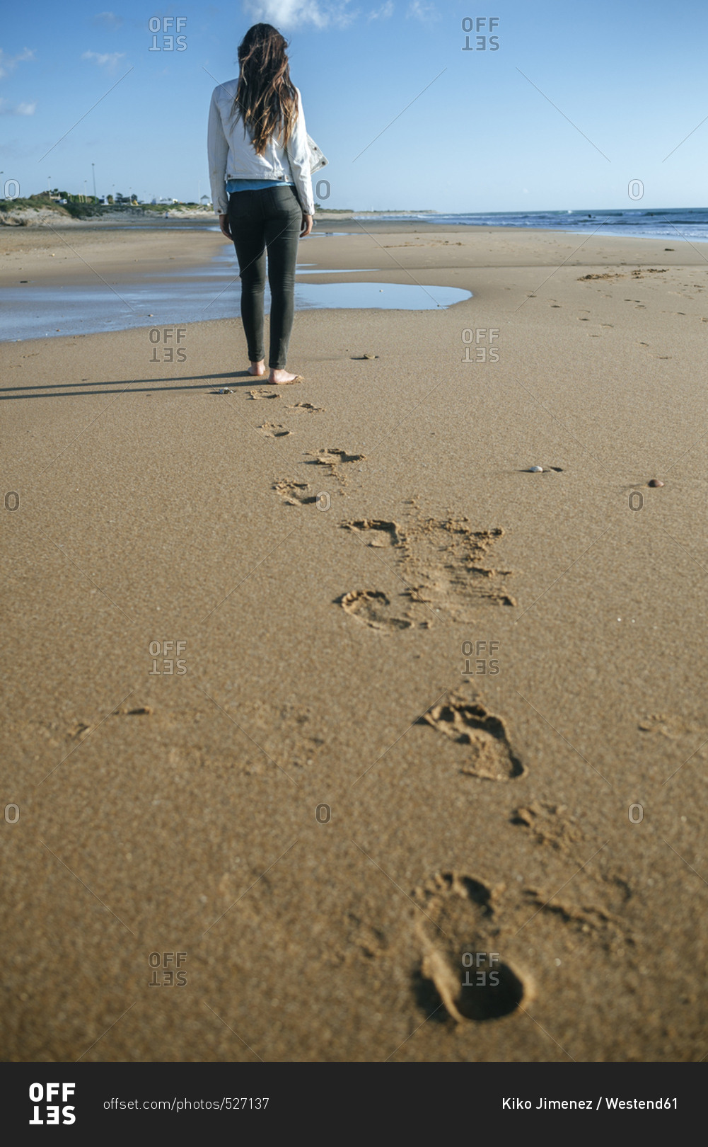 Back view of young woman walking on the beach leaving her footprints in the sand
