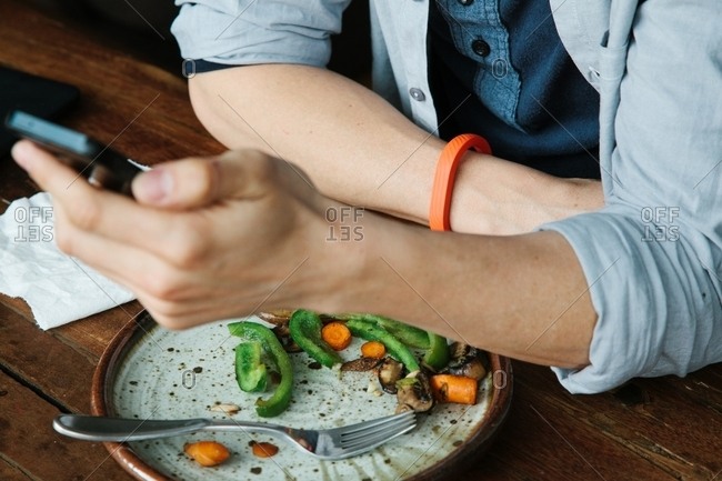 Man wearing fitness tracker and using cell phone while eating