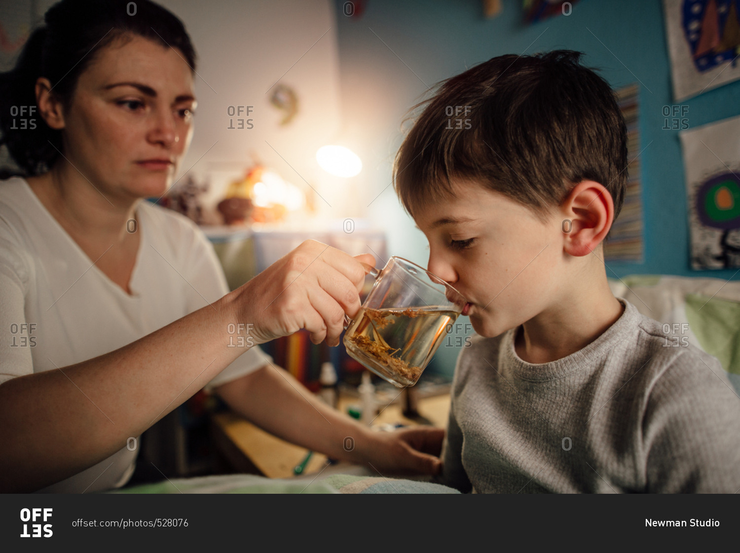 Child feeling unwell drinking a herbal tea from his mother