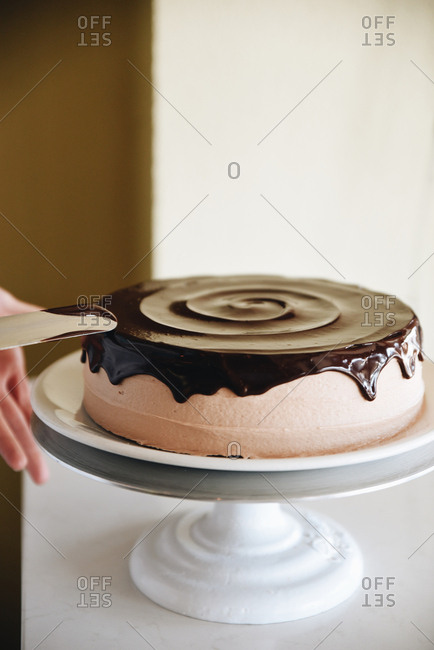 Person frosting a cake with chocolate ganache