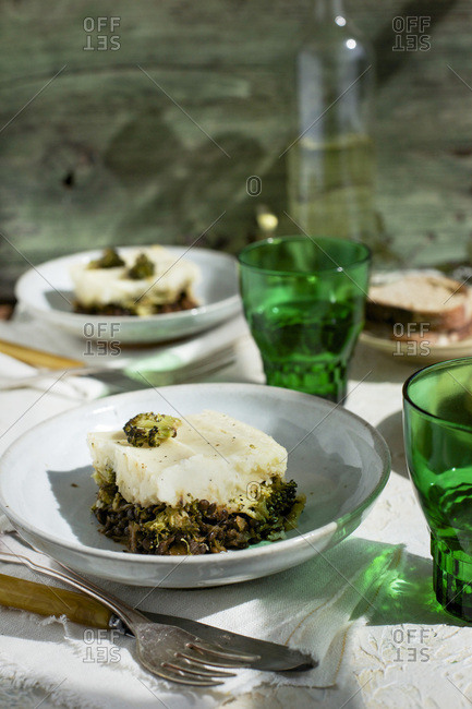 Black Lentil Charred Broccoli Shepherd's Pie served with bread and white wine. Photographed on white plaster background.