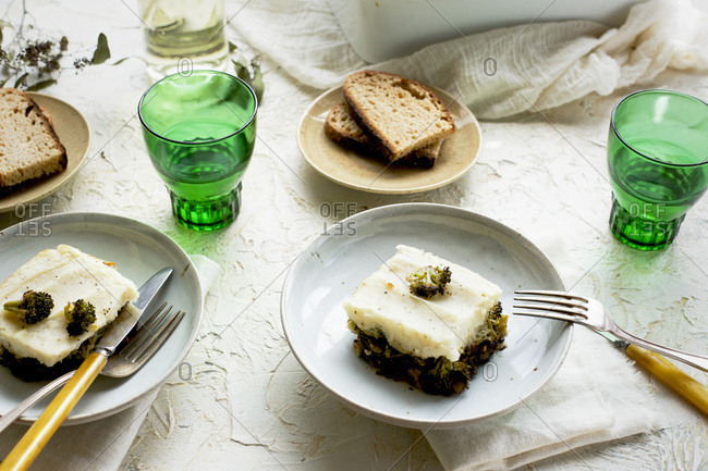 Black Lentil Charred Broccoli Shepherd's Pie served with bread and white wine. Photographed on white plaster background.