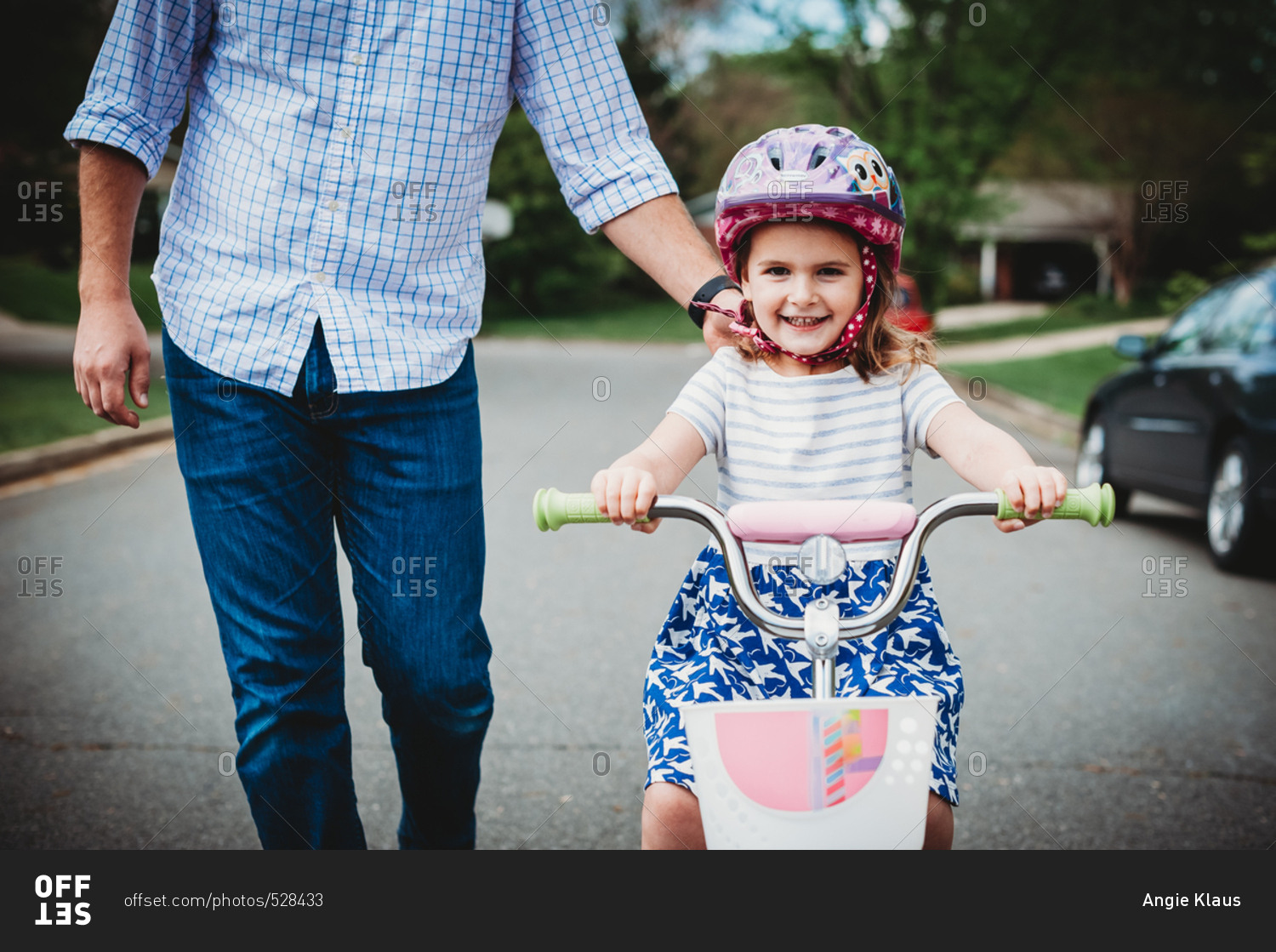 Father holding his daughter\'s shoulder as she learns to ride a bike