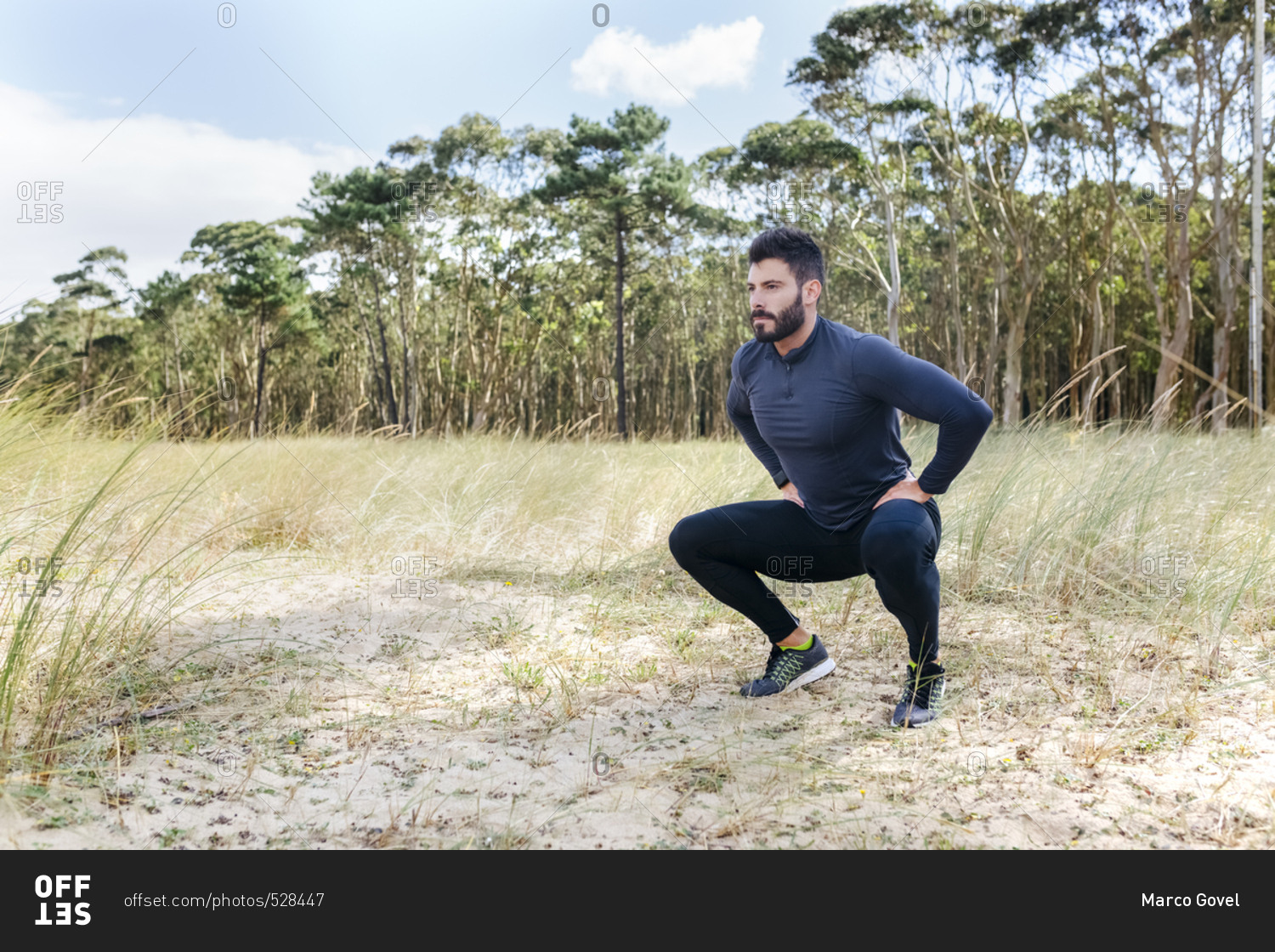 Athletic man squatting and stretching in the sand