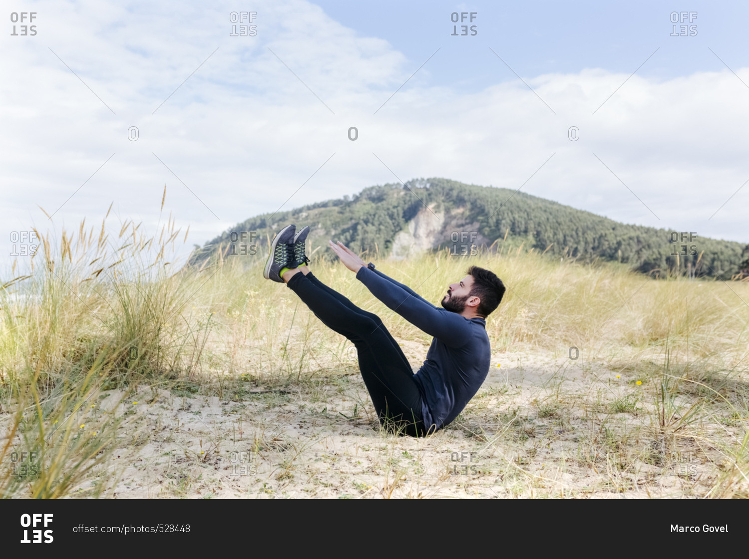 Athletic man sitting down and stretching in the sand