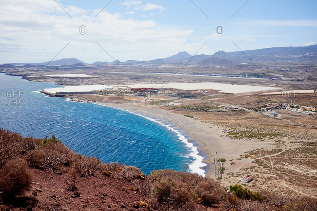 Lovely summer day in nature: deep blue water, empty seashore and high mountains on background, view from hill