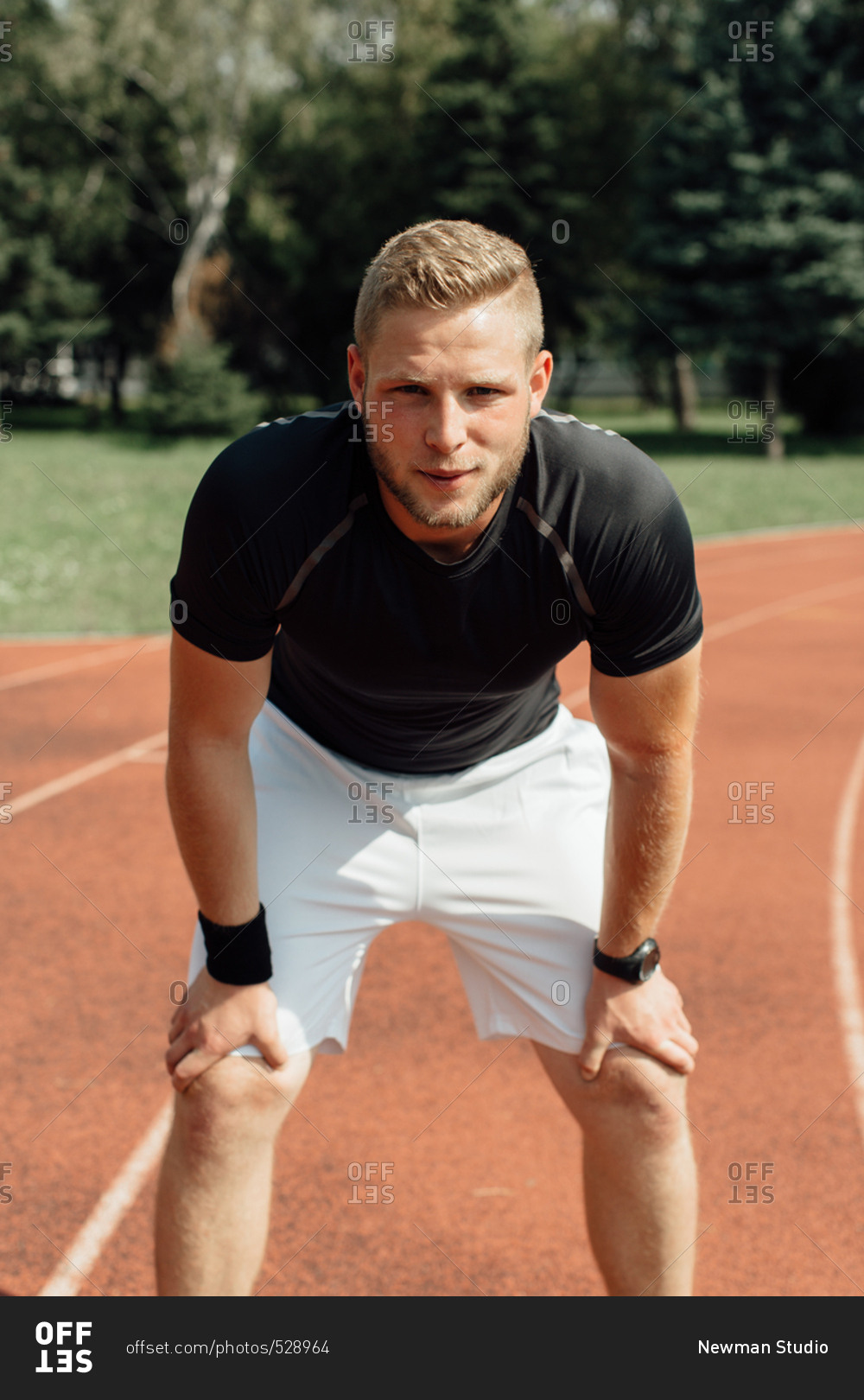 Front view of a male runner bending over and resting at a line stock ...