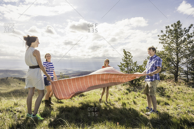 Young man and female friends preparing picnic blanket on hill, Bridger, Montana, USA