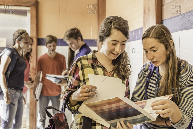 High school students reading notebooks in school corridor