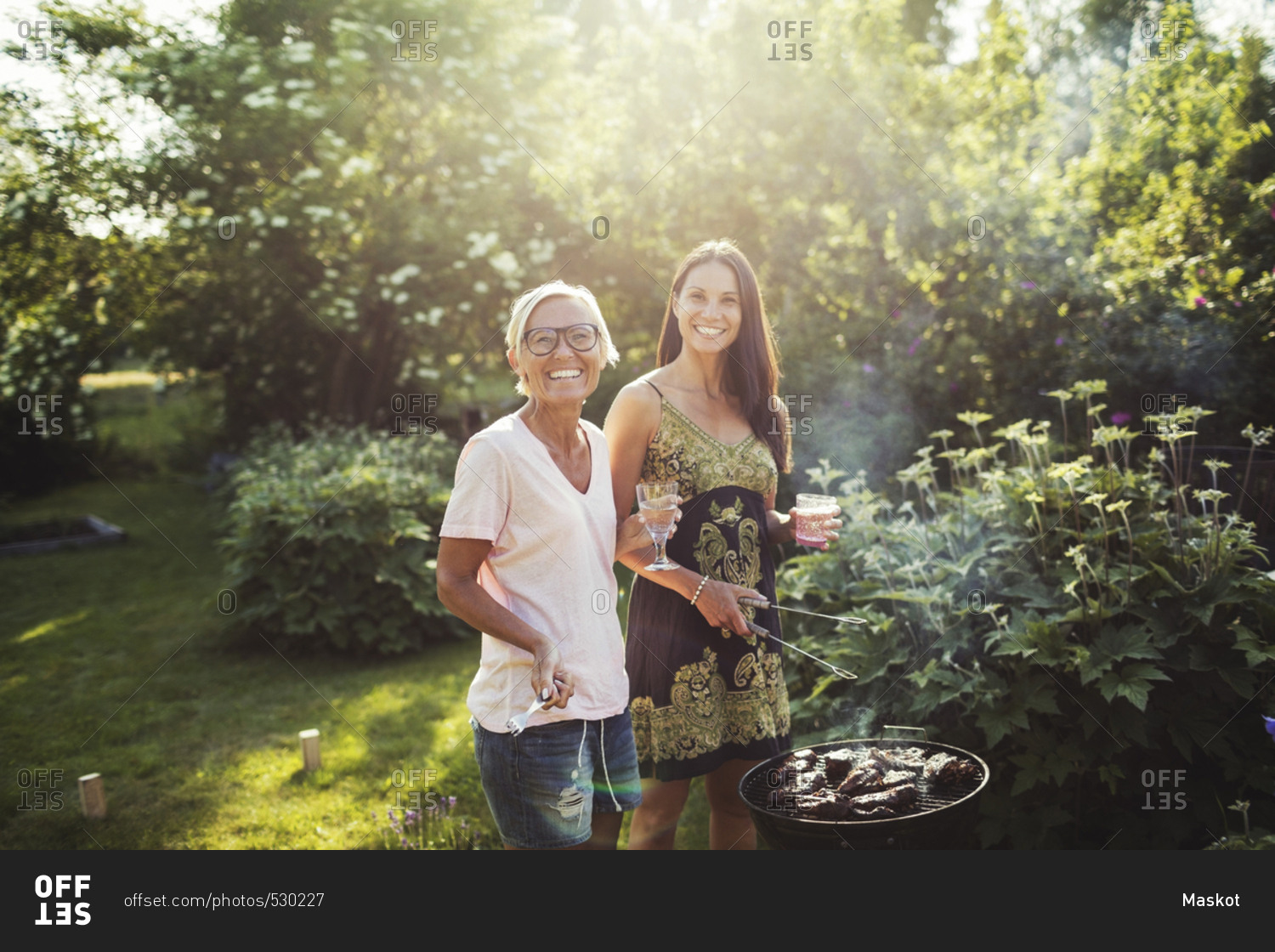 Portrait of happy women standing by barbecue grill at back yard on sunny day