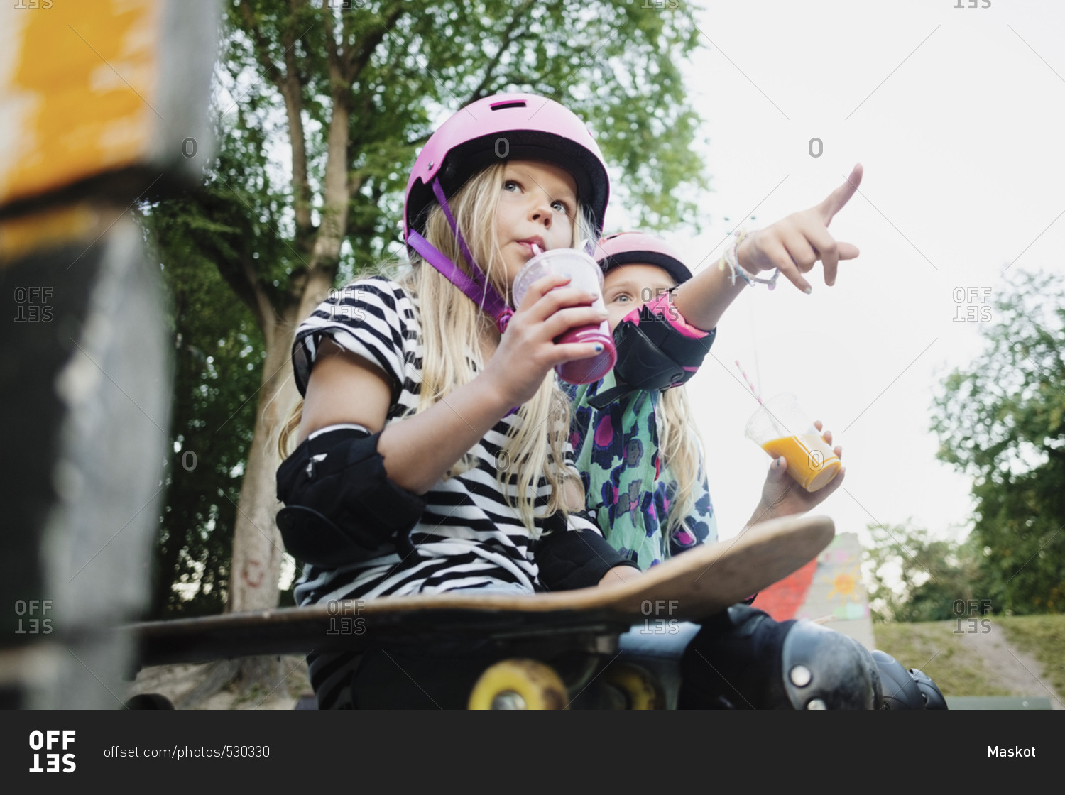 Girl pointing and showing to friend while having juice at skateboard park