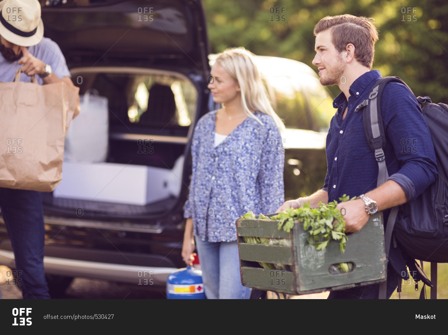 Man carrying wooden crate standing with friends by car