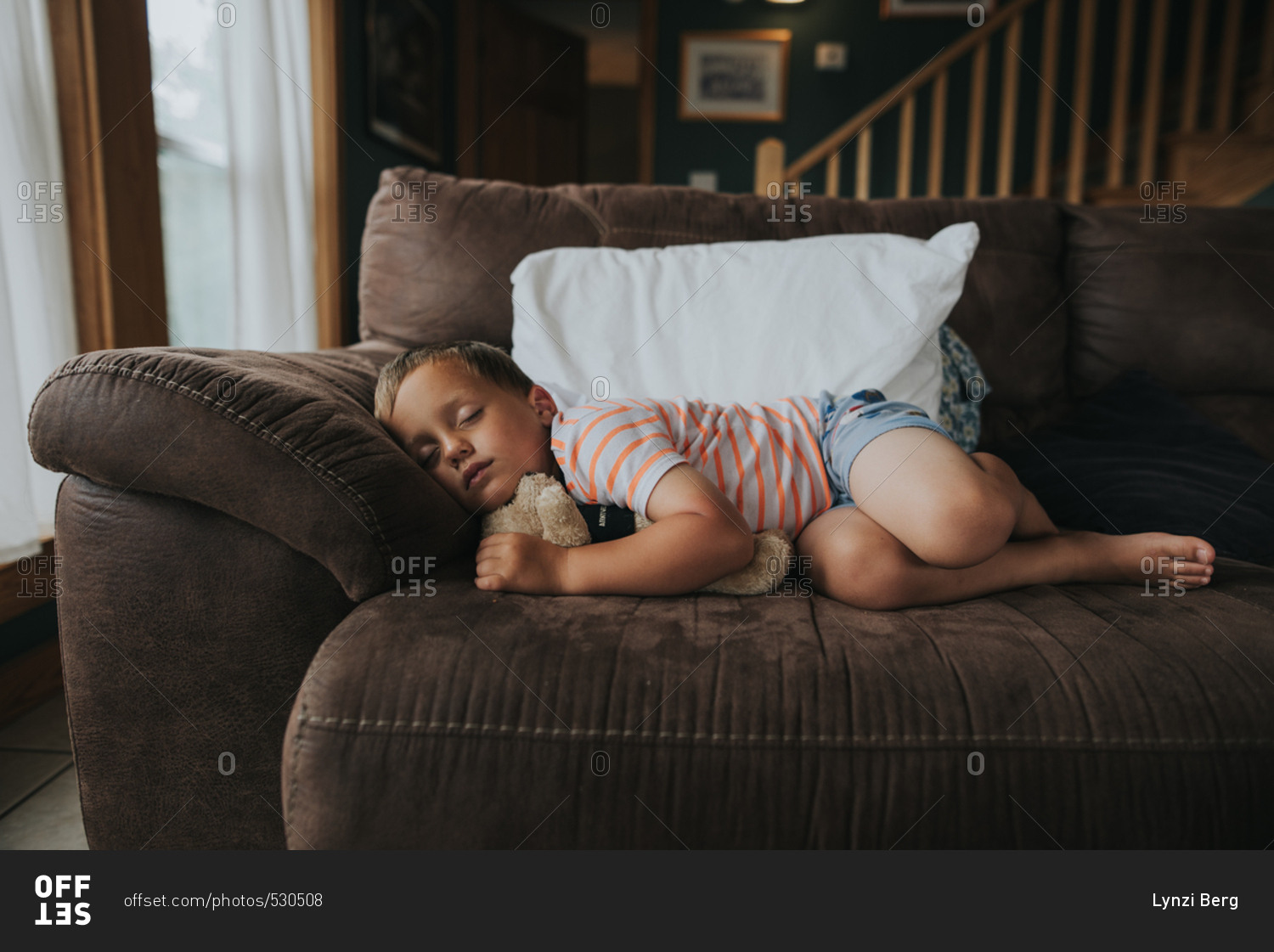 Little boy taking a nap with a teddy bear on a sofa