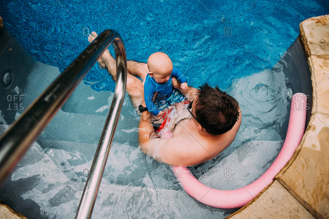 Father sitting on the steps of a swimming pool holding his infant son