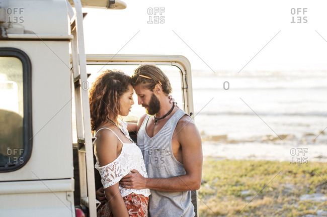 Couple romancing while standing by off-road vehicle at beach
