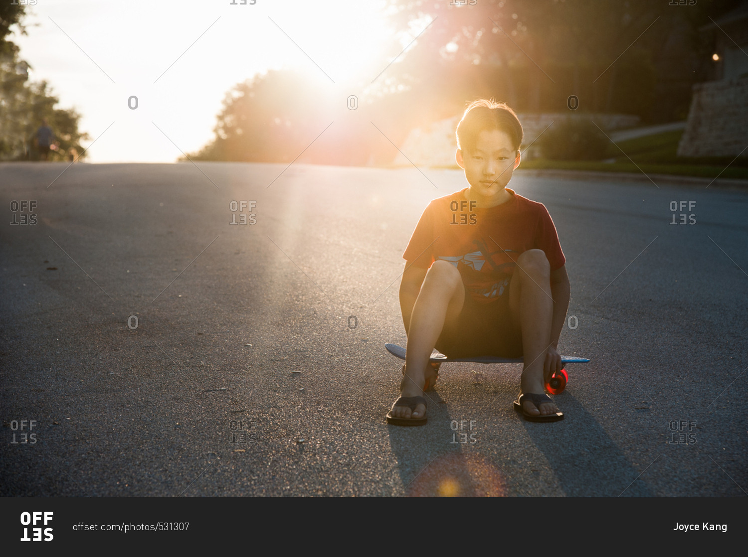 Portrait of an adolescent boy sitting on skateboard in street