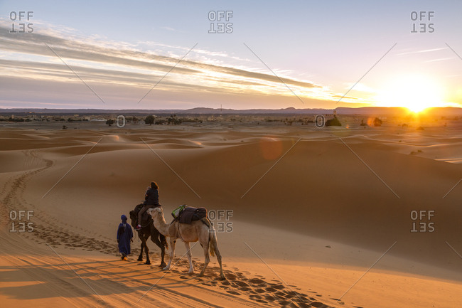 Merzouga, Morocco - November 24, 2016: Tuareg man with camels and tourists at the Erg Chebbi sand dunes, Sahara Desert