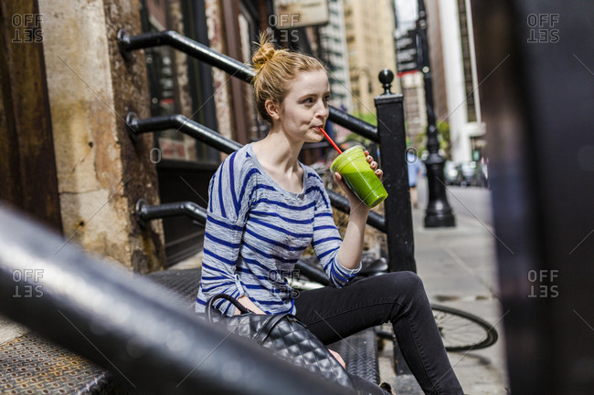 USA- New York City- woman sitting on stoop drinking a smoothie in Manhattan
