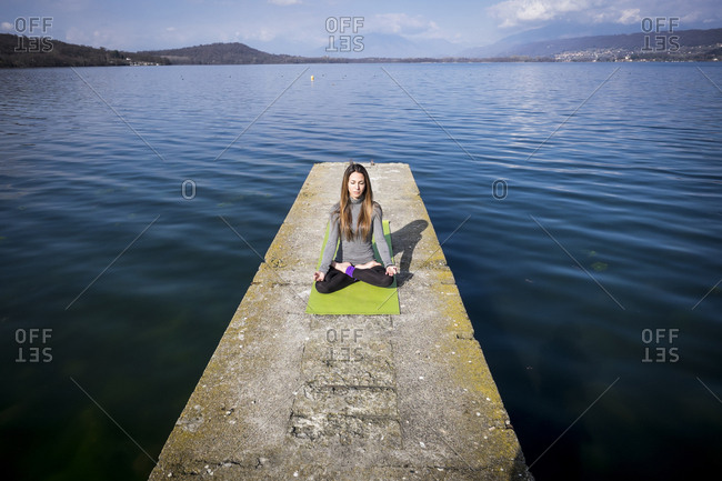 Woman practicing yoga on a pier at a lake