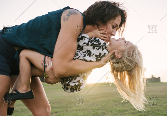 Mother bending over and kissing her daughter playfully in a field at sunset