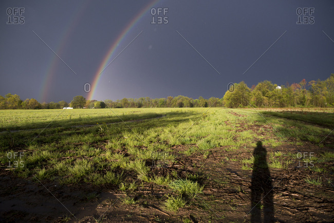 Double rainbow over countryside with person\'s shadow