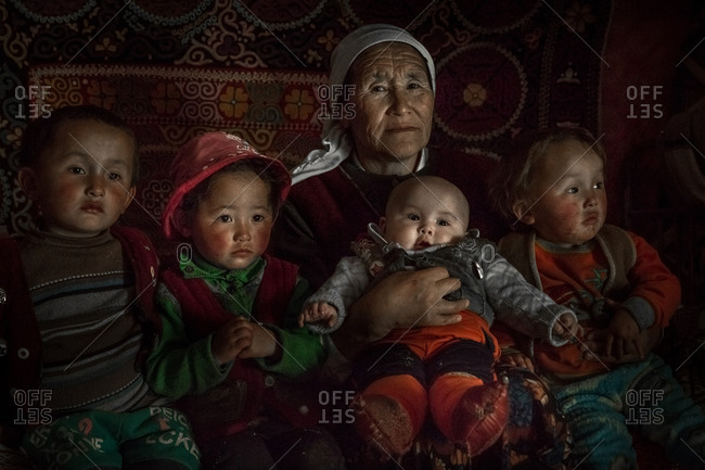 Altai Mountains, Mongolia - July 16, 2016: Senior Kazakh woman sitting on a bed with her grandchildren
