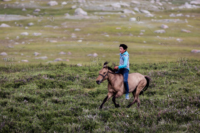 Altai Mountains, Mongolia - July 18, 2016: Young Kazakh boy on running horse