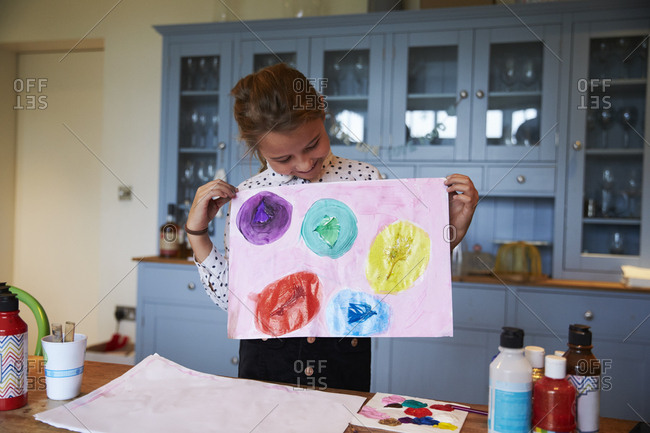 Girl at kitchen table holding picture she has painted