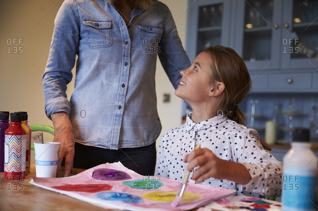 Mother watches as daughter paints picture at kitchen table