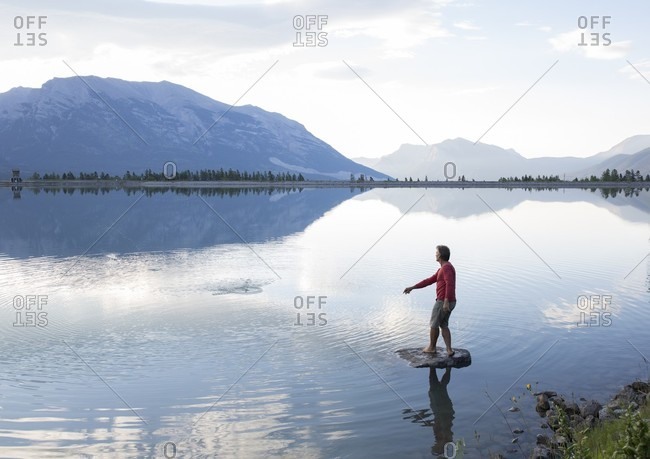 Man skips rock from island, mountains distant