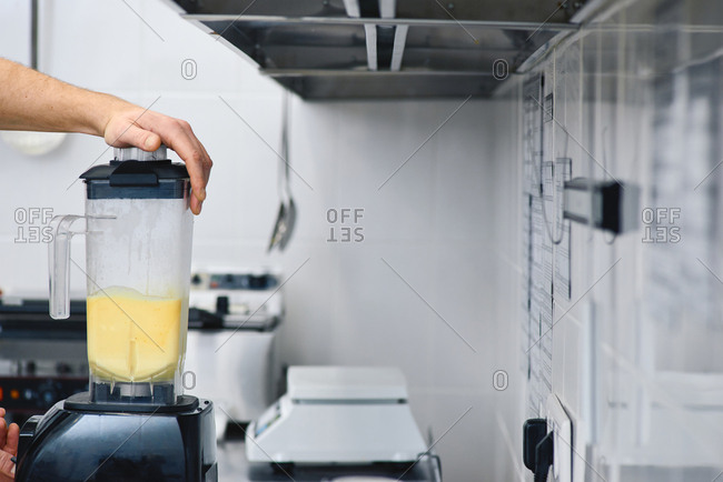 Preparing nutritious cocktail. Male hand holding blender lid while making citrus smoothie in restaurant kitchen, close-up view